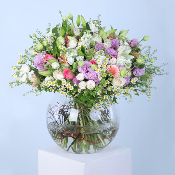 A vibrant bouquet of pink gerbera daisies, pink roses, white ohara lilies, and other colorful blooms, arranged in a glass vase