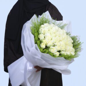 A large bouquet of 51 white roses wrapped in white paper with thalapsi green accents