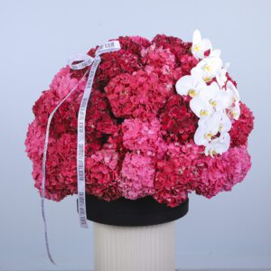 Pink and red hydrangeas with a smaller cluster of white phalaenopsis orchids on top, arranged in a black box.