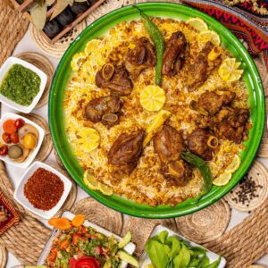 The image showcases a delicious-looking platter of Mandi, a popular Yemeni dish. The dish is made with fragrant basmati rice, tender pieces of meat, and a variety of spices and herbs. The platter is beautifully arranged on a green tray, surrounded by various side dishes and condiments.