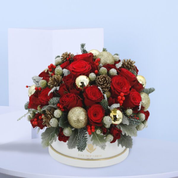 A Christmas arrangement in white box with red roses, gold ornaments, and pine cones.