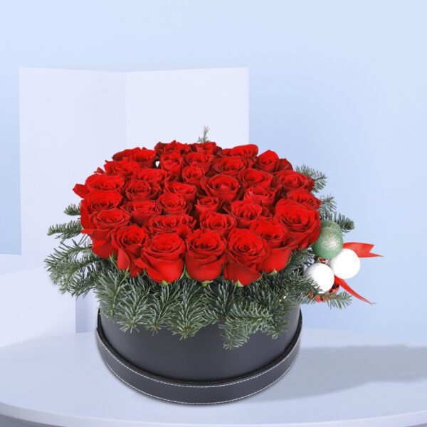 A Christmas flower arrangement in a black box with red roses and pine needles.