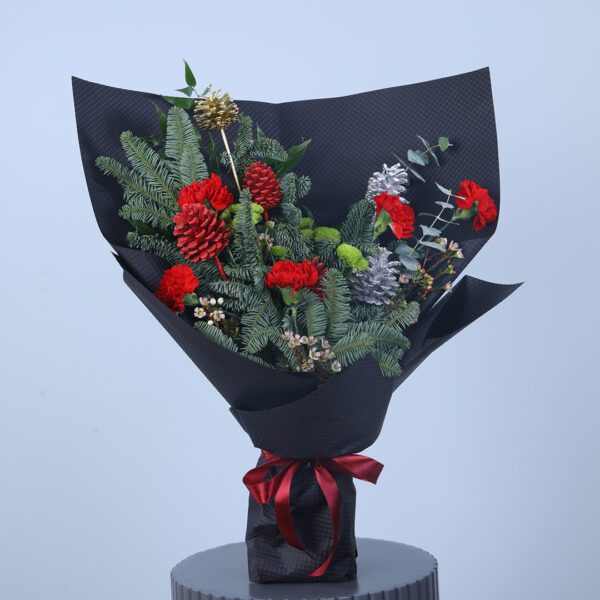 A modern Christmas bouquet with red carnations, silver accents, and lush greenery wrapped in black paper with a red ribbon.