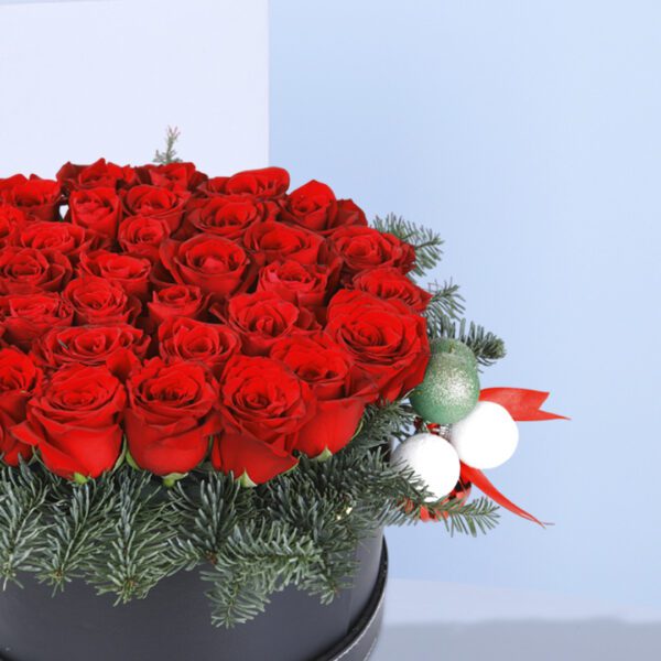 A Christmas flower arrangement in a black box with red roses and pine needles.