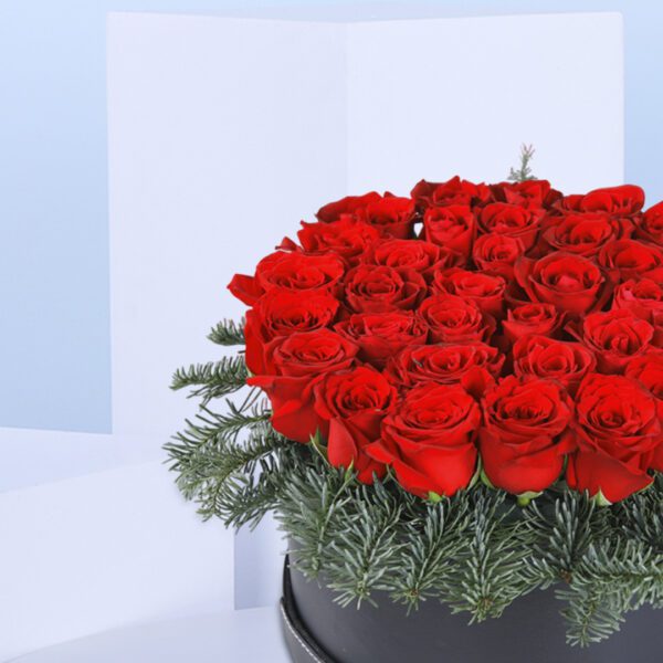 A Christmas flower arrangement in a black box with red roses and pine needles.