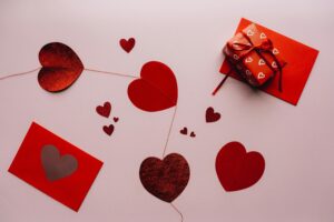 Several red paper hearts of varying sizes are scattered across a light pink background.